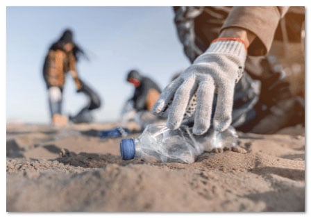 Hand in a glove picking up an empty water bottle from a beach