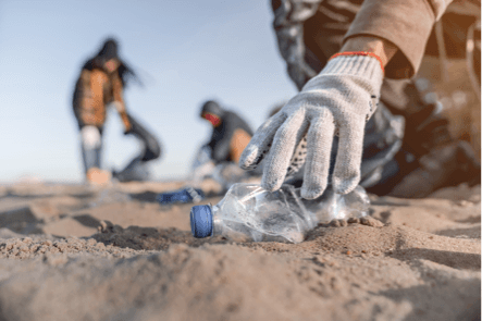 CSR: una mano con guanto prende una bottiglia di plastica da una spiaggia