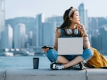 Woman sitting cross-legged in front of a city scape with a laptop and headphones