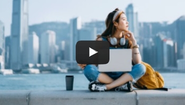 Woman sitting cross-legged in front of a city scape with a laptop and headphones