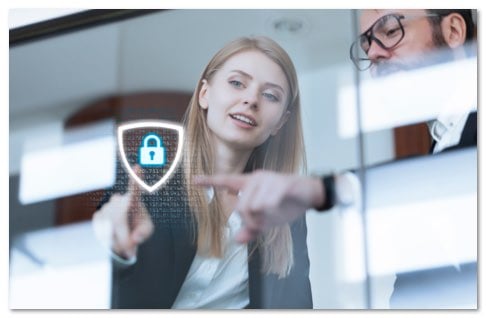 Blond woman and man with glasses pointing at a screen with a glowing lock icon inside of a shield