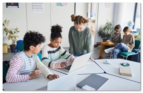 middle school children working around a laptop at a white table