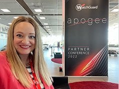Diana Harter in front of a WatchGuard Apogee partner conference banner