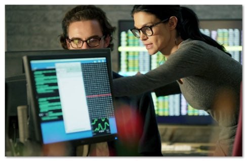 Woman and man in glasses talking about data on a monitor in front of them
