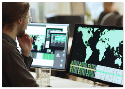 Person in glasses looking at a monitor with a global map on it in green