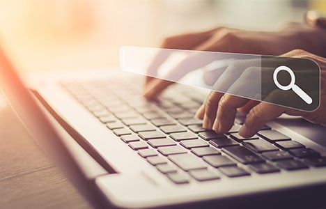 Hands typing on a laptop keyboard with a floating search field in front