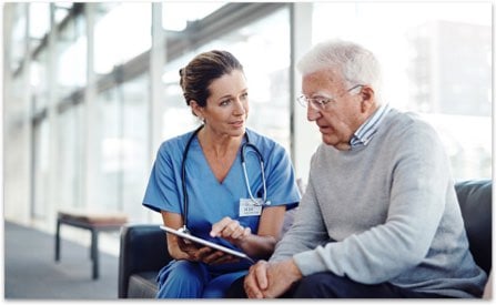 Doctor in blue scrubs showing information to an older gentleman on her tablet screen