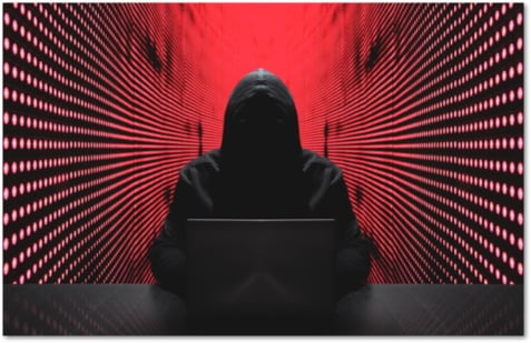 Shadowy figure in a hoodie using a laptop in a red walled room