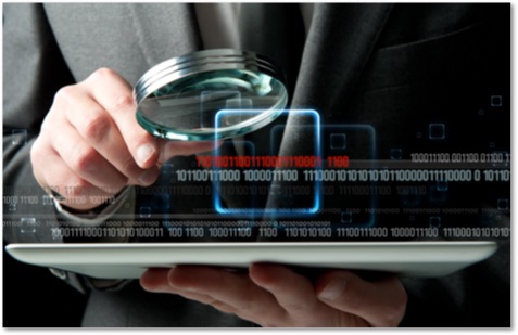 Man in a gray suit looking at a tablet computer through a magnifying glass