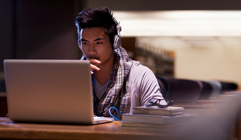 Teenager in headphones sitting at a long table looking at a laptop