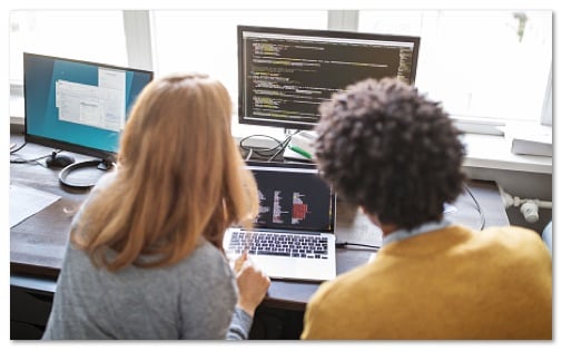 Students working at a laptop and monitor with code on the screen