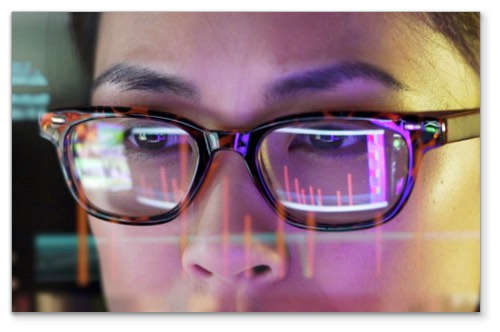 Closeup of person's face with monitors reflected in their glasses