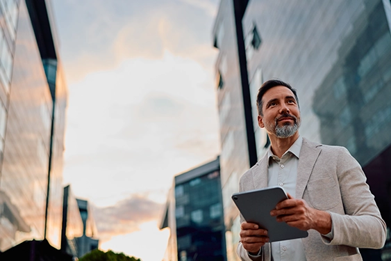 Man in a light suit walking between skyscrapers holding a tablet computer