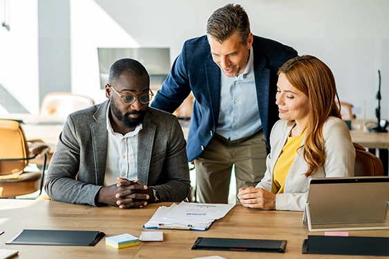 3 workers in an office looking at a document on the desk together
