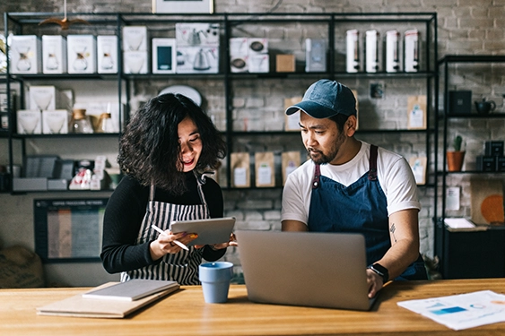 Man and a woman in aprons working on a laptop and tablet computer in a flower shop