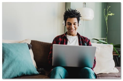 Teen boy sitting on a couch with headphones working on a laptop