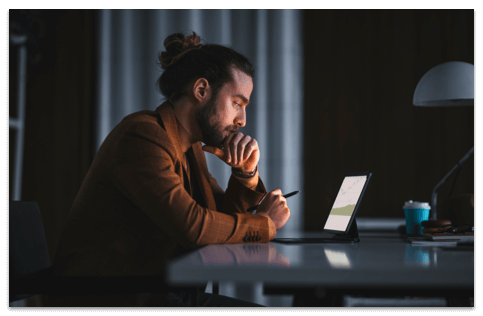 Bearded man in a brown long sleeve shirt working on a tablet in a dark room