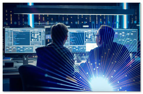 2 workers in front of 3 monitors with screens of code on them with a bright blue lens flare effect at the bottom right