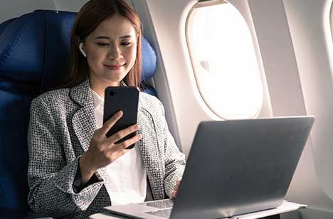 Woman in an airplane on her laptop looking at her phone