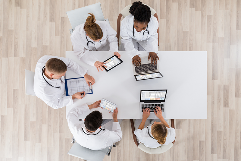Des médecins en blouse blanche assis autour d'une table avec des tablettes et des ordinateurs portables.