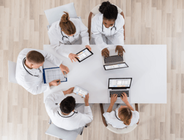 Foto: Menschen sitzen um einen Tisch an Ihren Computern, von oben aufgenommen