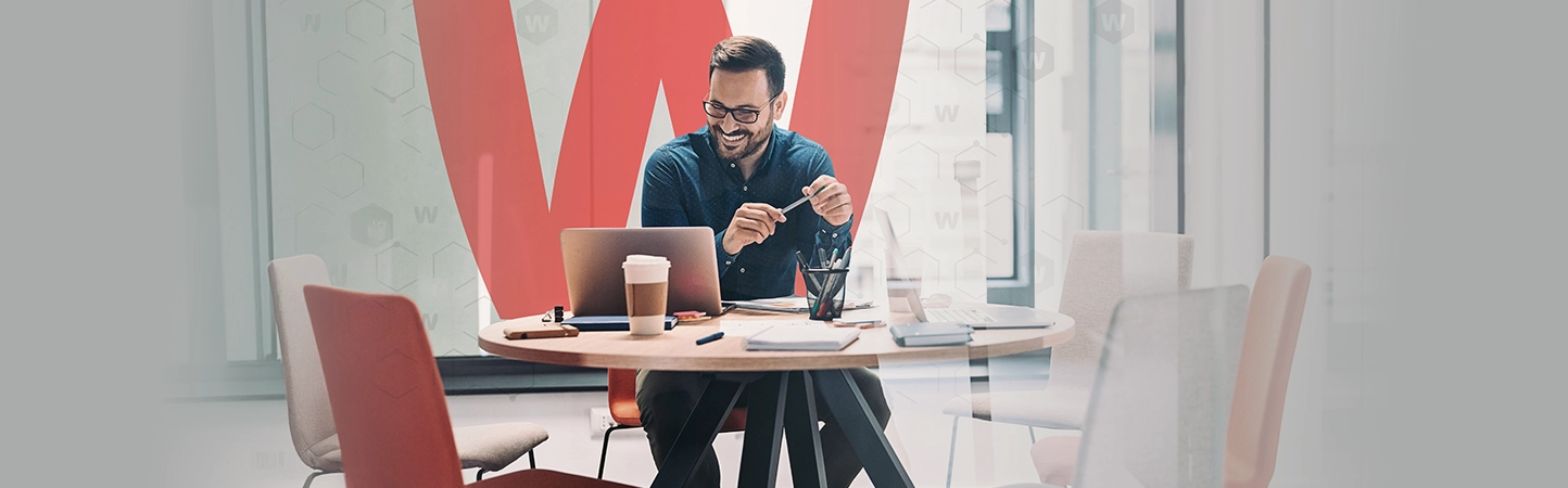 man in an open office smiling at his laptop
