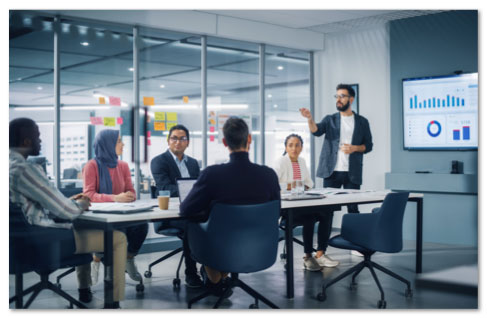 Business people meeting in a glass-walled conference room with a graph on screen at the front