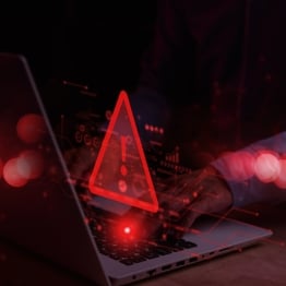  Cybersecurity warning symbol glowing red over a laptop keyboard, representing malware threats, malicious code, and cyberattack detection.