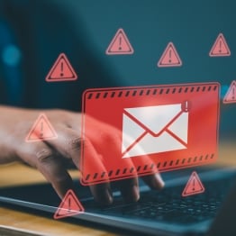 Person using a laptop with a warning overlay showing a suspicious email icon, representing a phishing or malware attack.