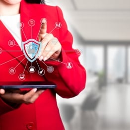 Business professional using a tablet with a digital cybersecurity shield and connected security icons overlayed on screen.
