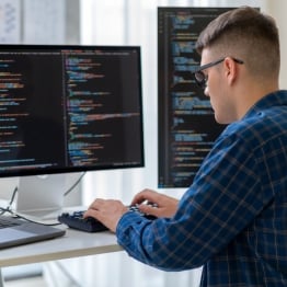 Developer working at a multi-monitor coding workstation with software code displayed across screens in a modern office environment.