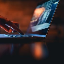 Person using a laptop in a dark setting, representing digital identity, AI access, and cybersecurity risk.