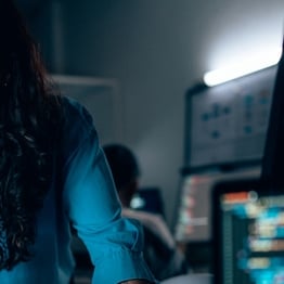Cybersecurity professional analyzing code on multiple monitors in a modern security operations center, investigating threats and system defenses.