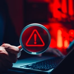Cyber threat detection and data risk warning concept. Person holding magnifying glass with digital alert symbol representing cybersecurity breach, malware investigation, system vulnerability analysis.