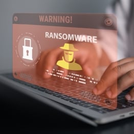 Businessman using laptop with ransomware warning alert and hacker icon. Concept of cyber attack, malware infection, data encryption threat, network security breach, and digital protection.