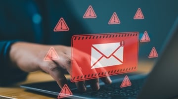 Person using a laptop with a warning overlay showing a suspicious email icon, representing a phishing or malware attack.