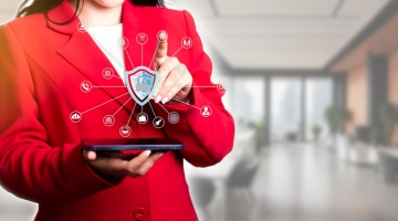 Business professional using a tablet with a digital cybersecurity shield and connected security icons overlayed on screen.