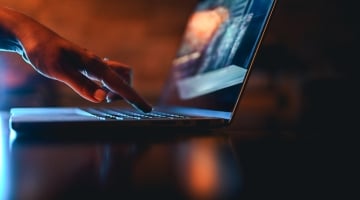 Person using a laptop in a dark setting, representing digital identity, AI access, and cybersecurity risk.
