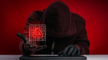 Hooded cybercriminal holding a glowing QR code with a warning symbol, representing QR code phishing, social engineering, and cryptocurrency cyber threats.