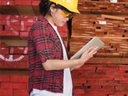 Woman at a worksite in a yellow hardhat looking at a tablet