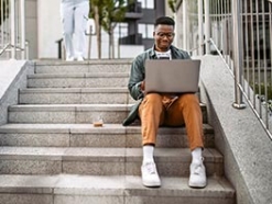 Young black man sitting on university steps working on a laptop