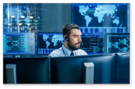 Man in a SOC surrounded by monitors and glowing maps on the walls