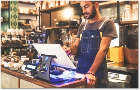 Man in a blue denim apron working at a bakery checkout terminal