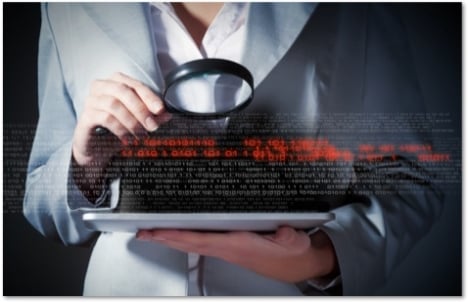 Person in a gray suit using a magnifying glass to look at code on a tablet computer