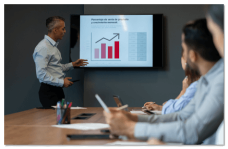 Man presenting in a meeting with a red bar graph on a large screen