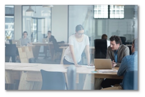 workers in an open office talking over a laptop