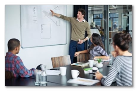 Man pointing at a white board with 3 co-workers looking on