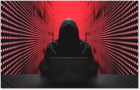 Shadowy figure in a hoodie using a laptop in a red walled room