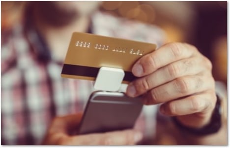 Man in a plaid shirt swiping a card through a square reader attached to a phone