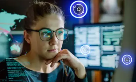 Woman in glasses surrounded by glowing maps and monitors